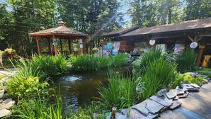 A garden with a pond, a wooden gazebo, and a building with signage. - The Springbrook  Inn - Forrest View Room (Hot Tub) (Denton Township)