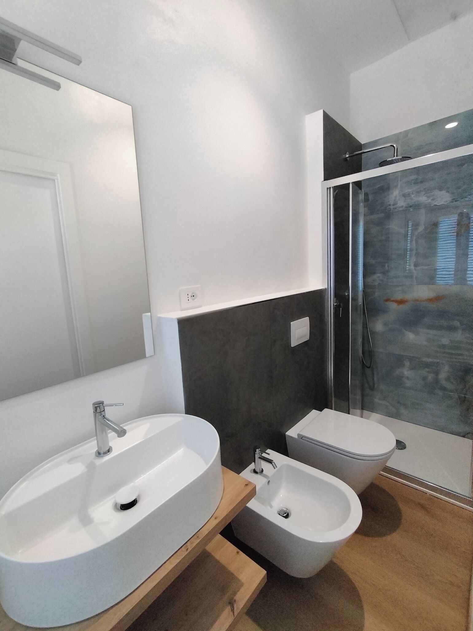 Une salle de bain moderne avec un grand lavabo blanc, un lavabo plus petit, un bidet et une douche à parois de verre.