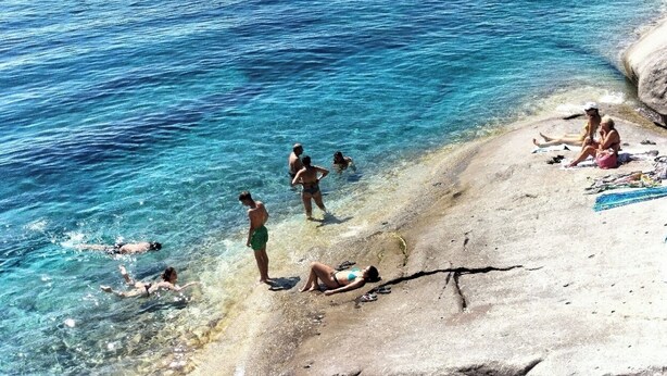 Una playa con agua azul cristalina, gente nadando y tomando el sol.
