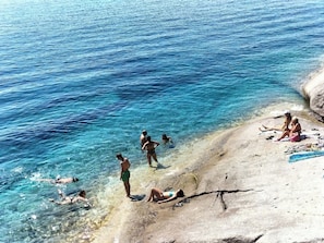 Una playa con agua azul cristalina, gente nadando y tomando el sol.