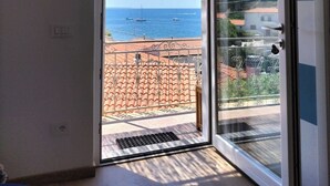 Una habitación con una puerta corrediza de vidrio que da a un balcón con vistas al mar y a barcos.