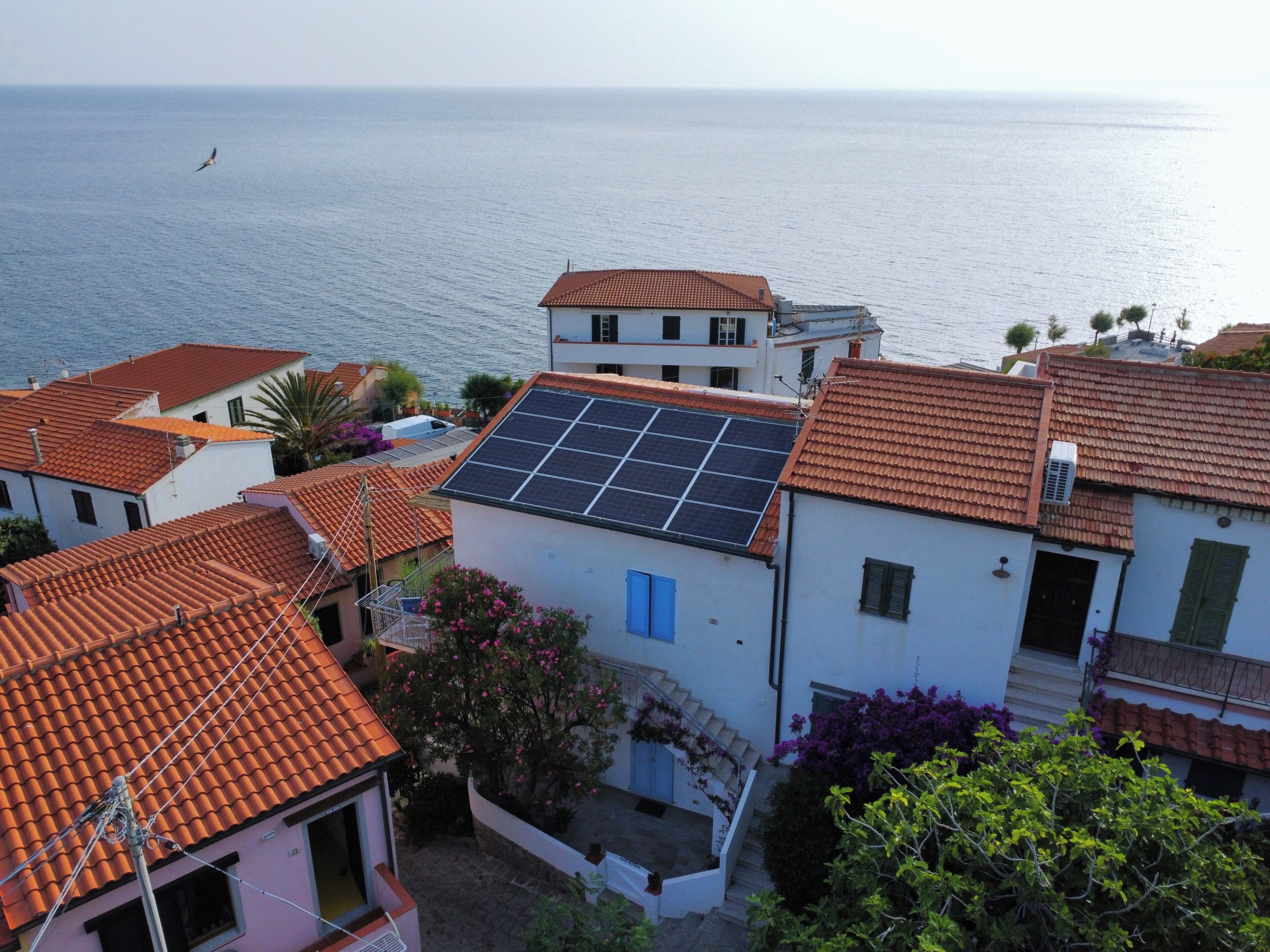 Un quartier résidentiel situé sur la côte, caractérisé par des toits recouverts de tuiles en terre cuite, des panneaux solaires et une vue sur la mer.