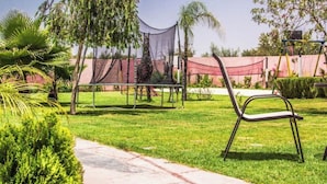 A grassy outdoor area with a chair, a pathway, and a netted enclosure. - Magnifique Villa Riad Marrakech Route Ourika (Marrakesh)