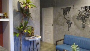 Une pièce avec un canapé bleu, une petite table sur laquelle se trouvent une plante et des fruits, et un mur décoré d’une carte du monde.