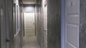 Un couloir étroit, avec des portes de chaque côté, qui mène à une porte centrale au bout.