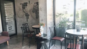 Un intérieur moderne avec un espace salon comprenant des tables et des chaises rondes, un mur décoratif orné de motifs textuels et une vue sur l’extérieur.