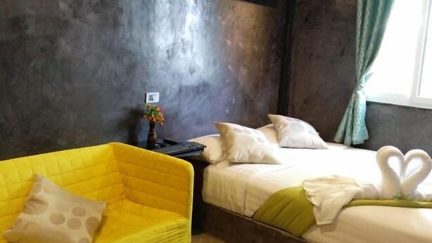 Une chambre d’hôtel avec un lit, un fauteuil jaune et une table de chevet sur laquelle se trouve un vase de fleurs.