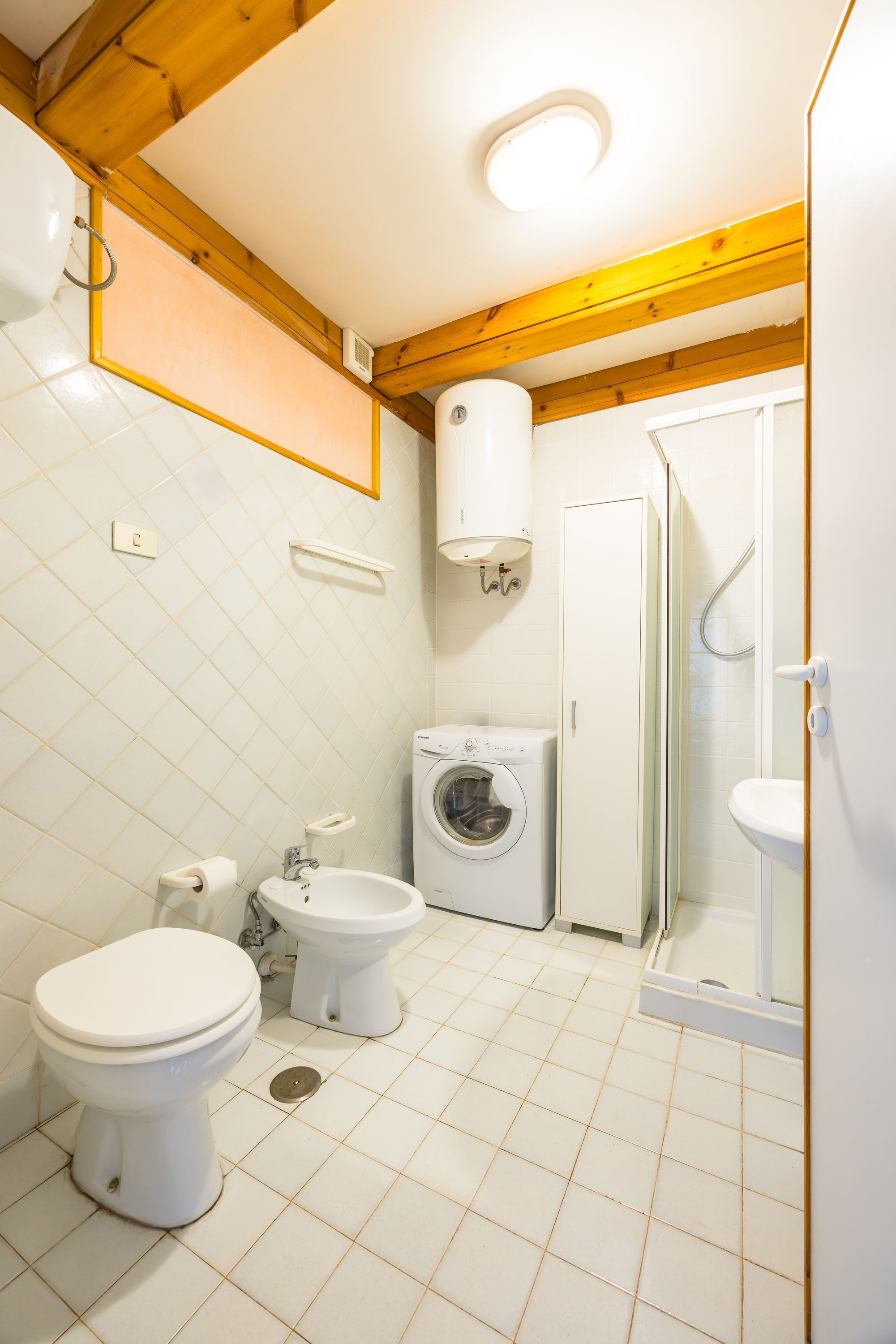 Une salle de bain équipée de toilettes, d’un bidet, d’un lave-linge et d’une douche à parois de verre.