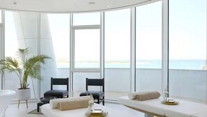 A modern spa room with two massage tables, a potted plant, and a view of the sea. - Ayia Napa Marina East Tower Suite (Ayia Napa)