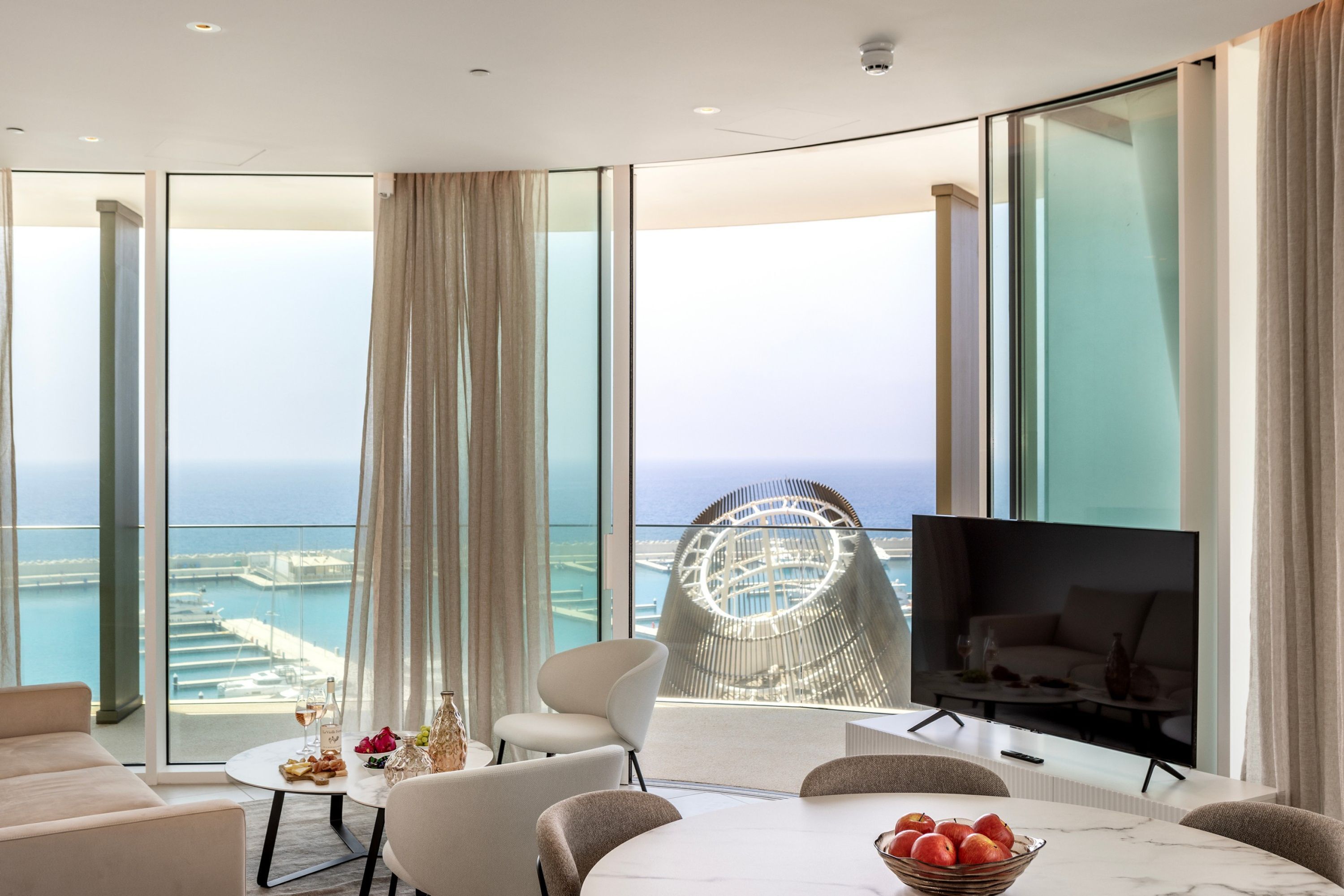 Un salon moderne doté d’un grand téléviseur, de sièges confortables, d’une table à manger et offrant une vue sur la mer.