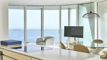 Una habitación moderna y bien iluminada con un amplio ventanal, un televisor de pantalla plana y una mesa de comedor de vidrio.