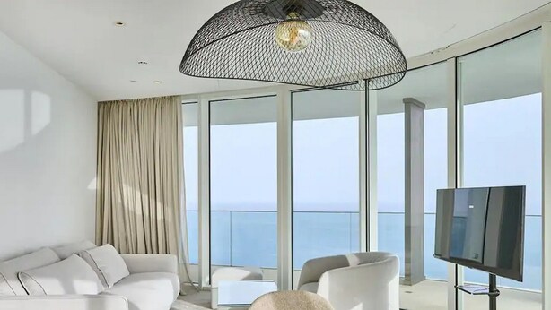 A modern living room with a glass table, white sofas, and a large window overlooking the sea. - Ayia Napa Marina East Tower Suite (Ayia Napa)