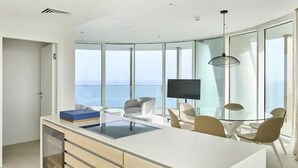A modern kitchen with a large island, a dining area with chairs, a TV, and a view of the ocean. - Ayia Napa Marina East Tower Suite (Ayia Napa)