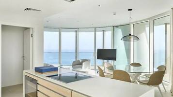 Una cocina moderna con una isla grande, un comedor con sillas, un televisor y vistas al océano.