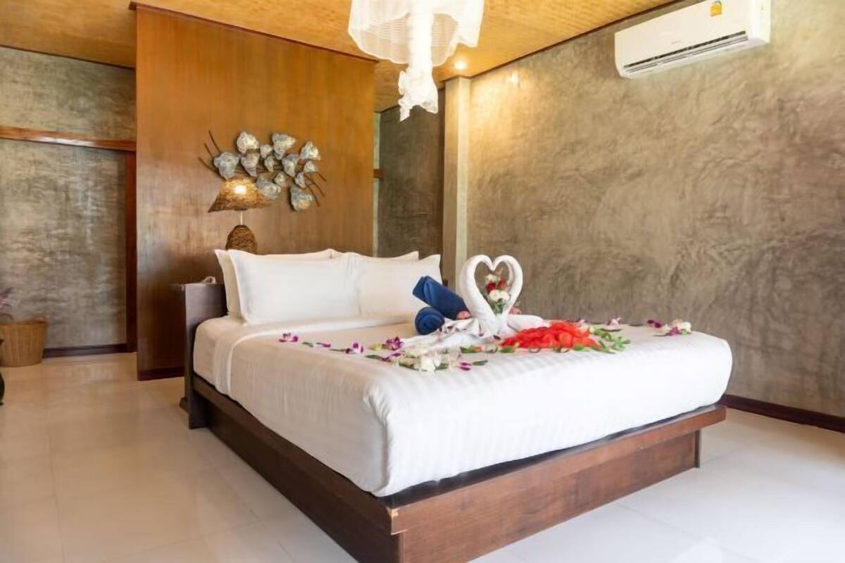 Un lit recouvert d’une couvre-lit blanche, un élément décoratif mural et une décoration en forme de cœur posée sur le lit.