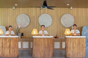 A reception desk with two staff members, wooden panel walls, and round wall decorations. - Long Beach Chalet (Koh Lanta)