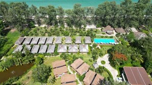 Eine Vogelperspektive zeigt ein Resort mit mehreren Bungalows, einem Schwimmbad und üppiger tropischer Vegetation.