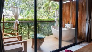 Ein Balkon mit Glastisch, Badewanne in Weiß und Holzmöbeln.