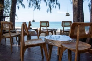 A wooden deck with chairs and tables, overlooking a beach with the ocean in the background. - Long Beach Chalet (Koh Lanta)