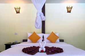 A hotel room with a neatly made bed, two pillows, a bedside table, and a wall-mounted light fixture. - Long Beach Chalet (Koh Lanta)