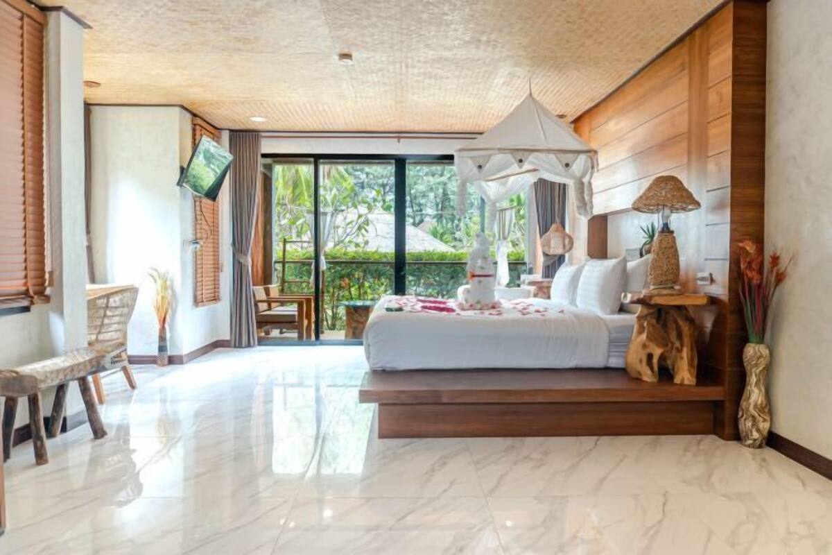 Une chambre dotée d’un grand lit, d’une télévision, d’un coin repas et offrant une vue sur la verdure environnante.