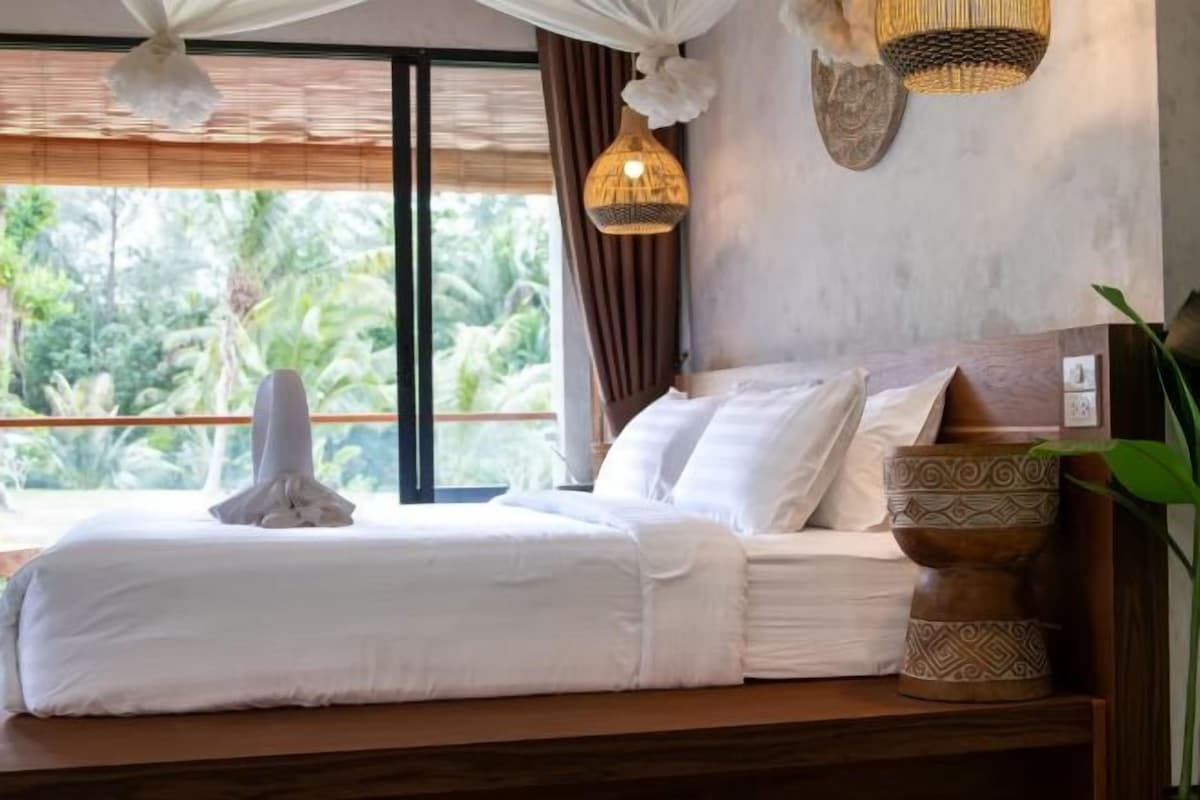 A bedroom with a bed, a window, and a bedside table with a plant.