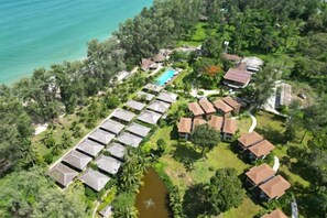An aerial view of a resort with multiple bungalow-style accommodations, a swimming pool, and a natural setting with a body of water and lush greenery.