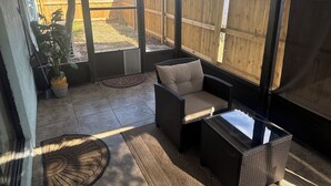 A covered patio with wicker furniture, a potted plant, and a view of a wooden fence. - Charming 3-bedroom house in wonderful Melbourne with WiFi, AC (Melbourne)
