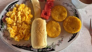 A plate with scrambled eggs, a sandwich, watermelon, and fried plantains on a floral-patterned plate. - CABAÑAS PLAYA TIBURON (Coveñas)