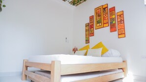 A bed with a wooden frame and white bedding, a wall with colorful artwork, and a small plant on the left. - CABAÑAS PLAYA TIBURON (Coveñas)