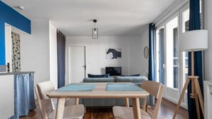 Una sala moderna con comedor, suelo de madera, un conjunto de sofás y un amplio ventanal con cortinas.