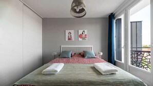 Un dormitorio moderno con una cama grande, dos almohadas, una mesita de noche, una lámpara colgante y un balcón con barandilla.