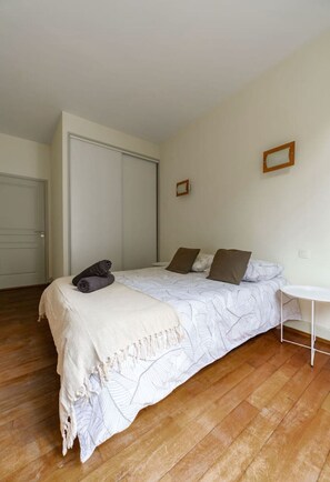 Un dormitorio con una cama, una mesita de noche, una silla, un armario y una puerta.