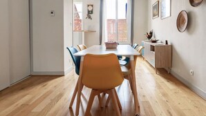 A modern dining area with a wooden table and chairs, a hanging light fixture, and a view of the kitchen through a window. - 2-bedroom designer apartment, Thermes district (Vichy)