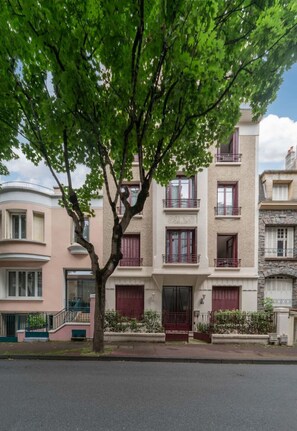 Un edificio residenziale a più piani con un ingresso centrale, balconi e un albero di fronte.