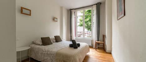 Un dormitorio con cama, una silla, una mesita y un ventanal con vistas a zonas verdes.