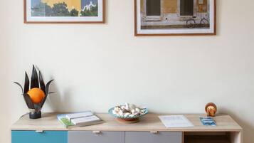 A modern, two-tiered wooden and grey cabinet with a teal accent drawer, a small orange sculpture, a bowl of mushrooms, and two framed artworks on the wall.