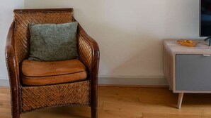 A room with a wicker chair, a television on a cabinet, and two framed pictures on the wall. - 2-bedroom designer apartment, Thermes district (Vichy)