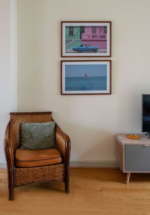 Una habitación con una silla de mimbre, un televisor sobre un mueble y dos cuadros en la pared.