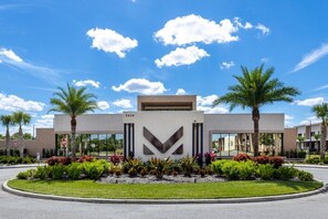 A modern building with a large 'V' logo, surrounded by palm trees and landscaped gardens.