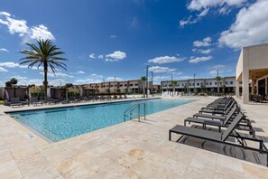A swimming pool with lounge chairs and a palm tree, surrounded by buildings.