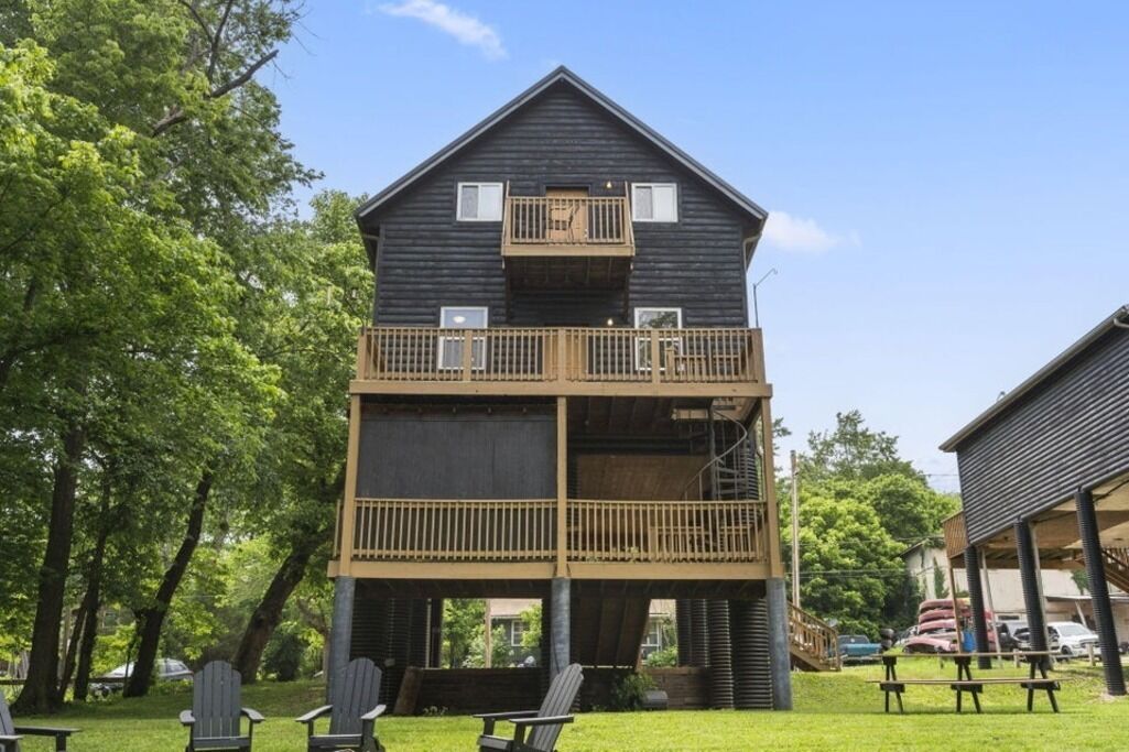 Un bâtiment en bois à deux étages, doté d’un balcon à l’étage supérieur, entouré d’arbres et agrémenté de sièges extérieurs.