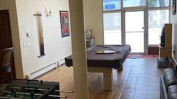 Ein geräumiges Wohnzimmer mit Kicker- und Billardtisch sowie einem großen Fenster mit Blick ins Freie.
