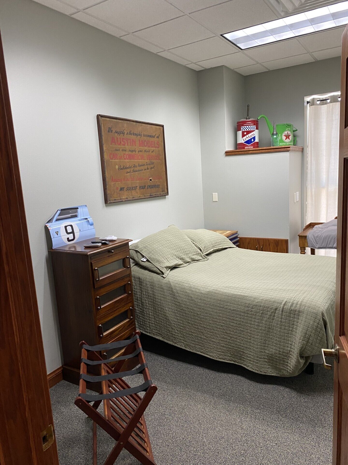 Een slaapkamer met een bed, een dressoir, een stoel, een bureau met een computer, en een bord aan de muur.