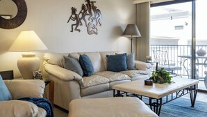 A modern living room with a beige sofa, a coffee table, and a balcony with outdoor furniture. - Fountain Hills Golf Condo | Heated Pool & Hot Tub (Fountain Hills)