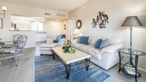 A living room with a sofa, coffee table, and a dining area with chairs. There is a kitchen in the background. - Fountain Hills Golf Condo | Heated Pool & Hot Tub (Fountain Hills)