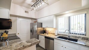 A modern kitchen with white cabinets, a stainless steel refrigerator, a dishwasher, and a granite countertop. - Fountain Hills Golf Condo | Heated Pool & Hot Tub (Fountain Hills)