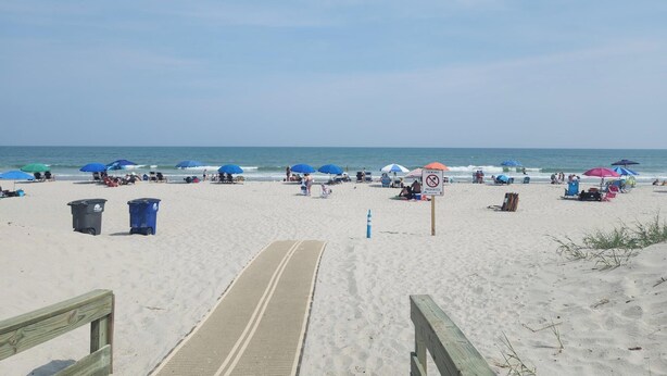 A beach with a wooden walkway leading to the water, beach chairs, umbrellas, and a sign prohibiting fireworks. - Charming 3-bedroom house with WiFi, AC in marvelous Myrtle Beach (Myrtle Beach)