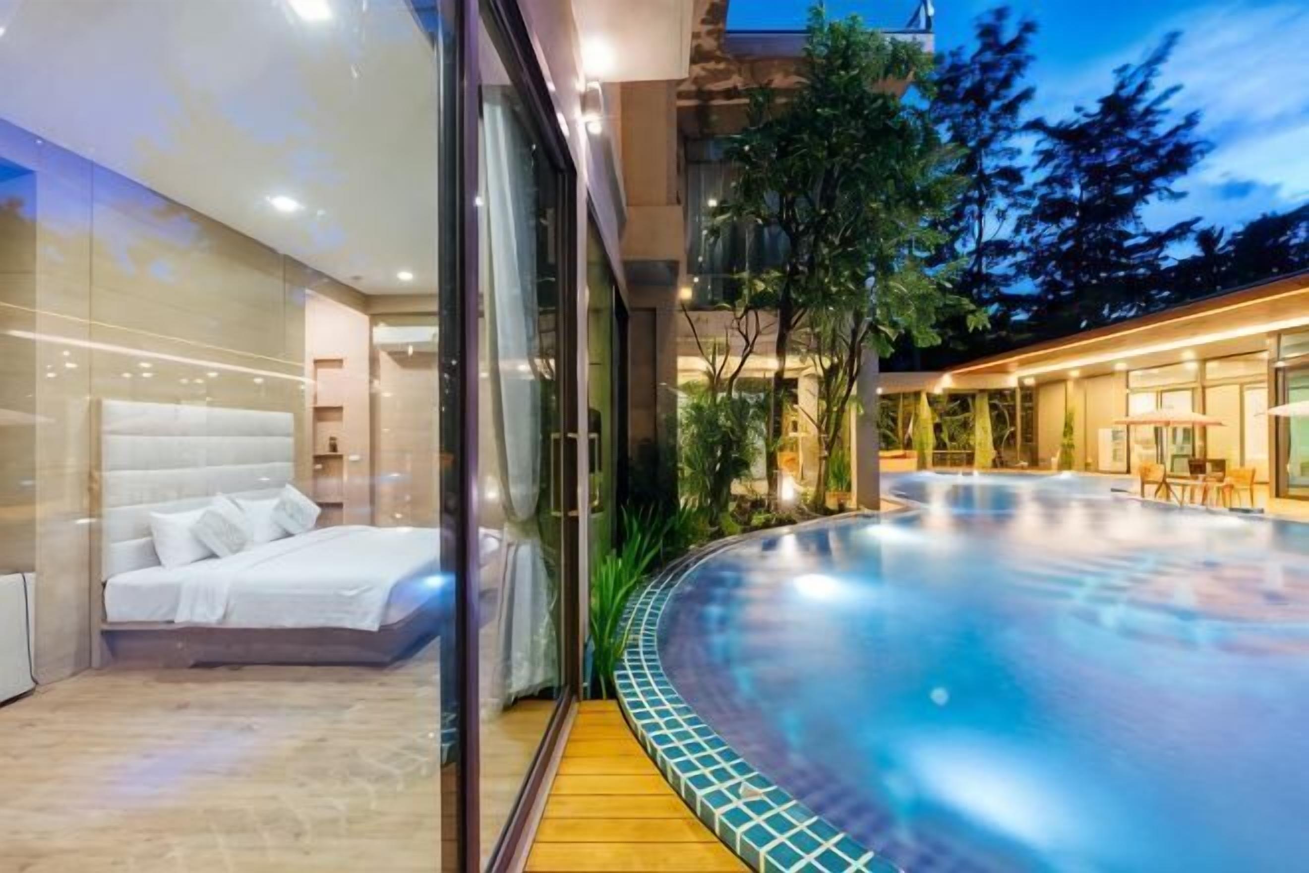 A modern bedroom with a large bed, a glass wall, and a view of a heated outdoor pool area.