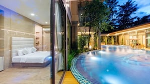 Camera moderna con un ampio letto, una parete di vetro e vista su un’area piscina esterna riscaldata.